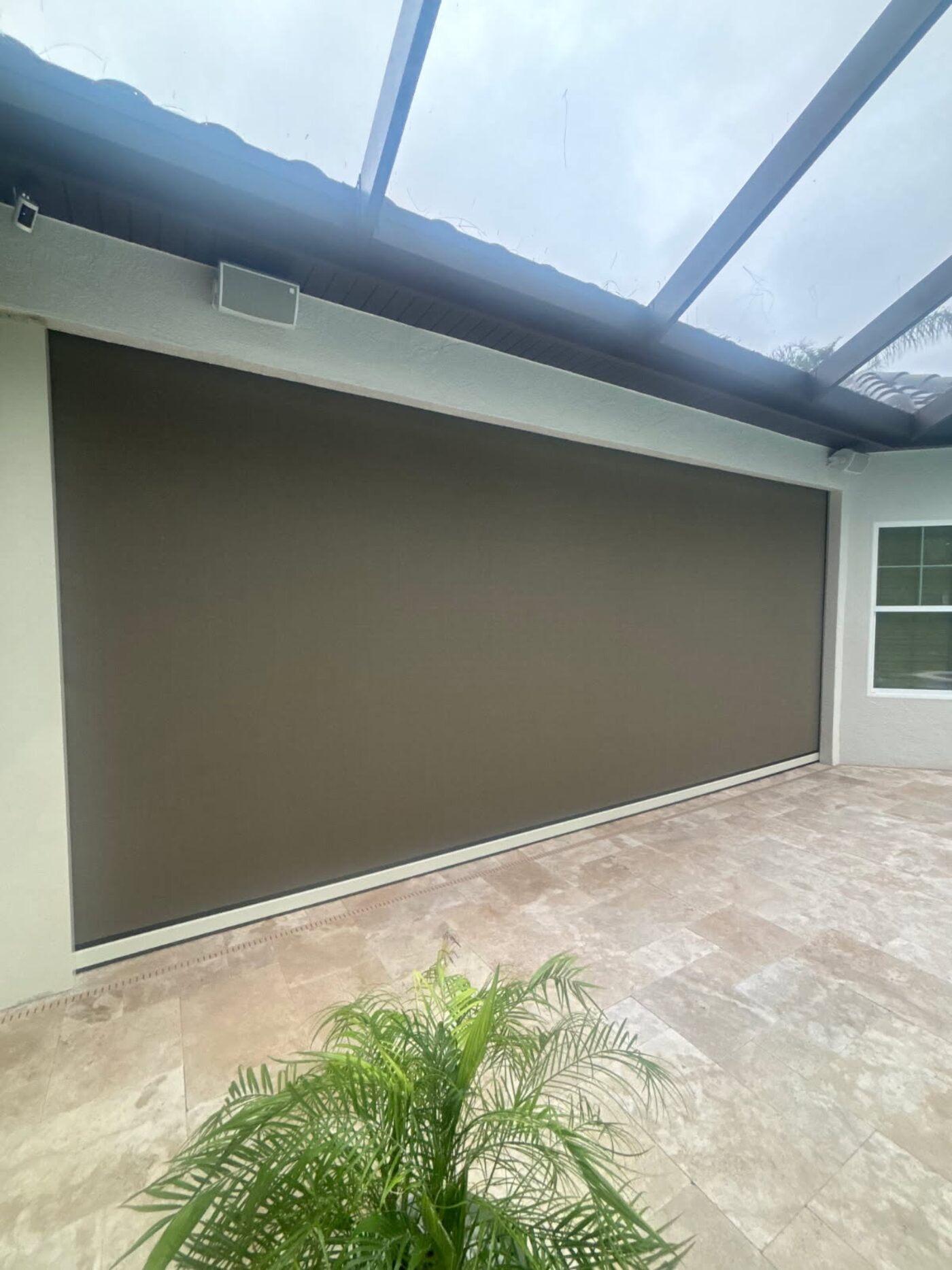 Large motorized retractable screen on a covered lanai with travertine pavers