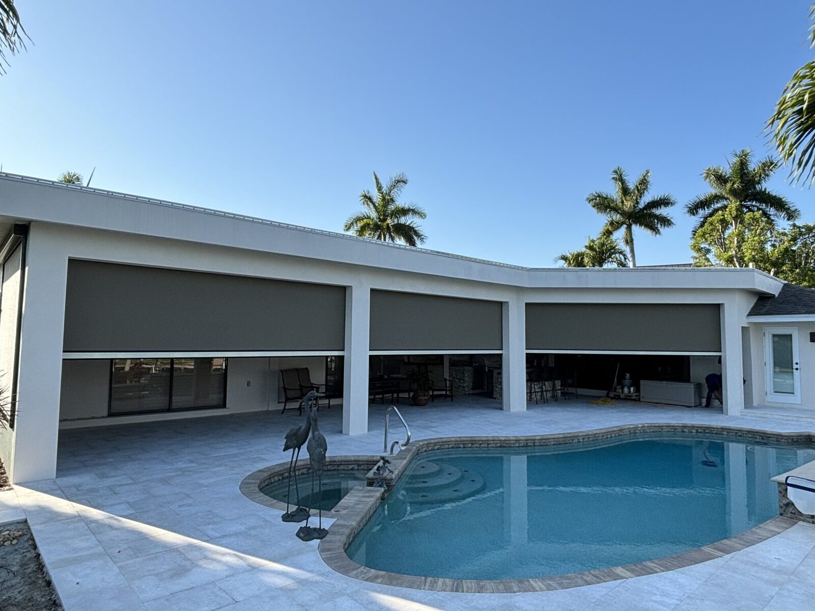 Wide lanai with three motorized retractable screens deployed over pool deck